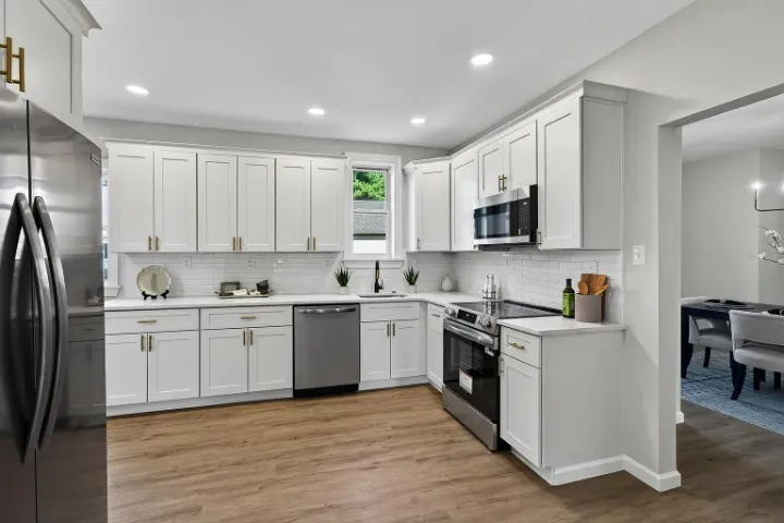 Renovated kitchen with white shaker cabinets, brass pulls, and stainless appliances